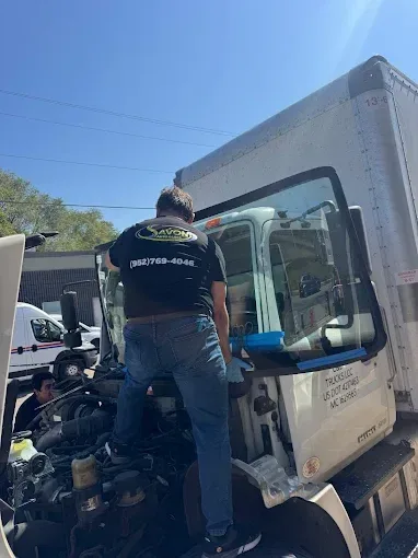 Mechanic in dark shirt standing at cab door of commercial box truck during daytime service