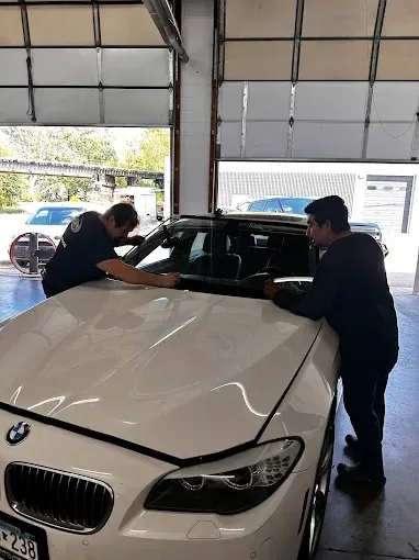 Two technicians installing a car cover on a white BMW in a garage