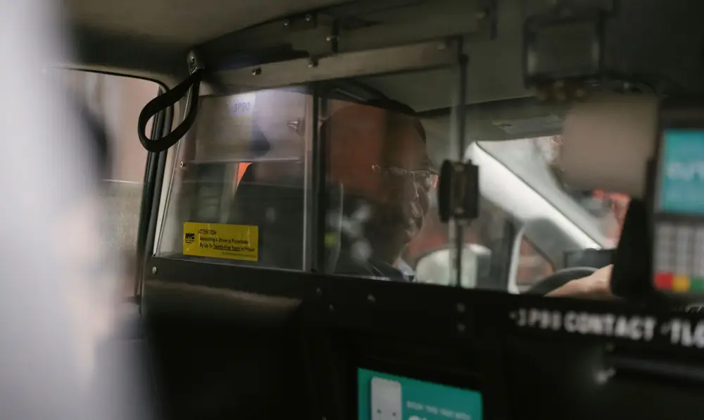 Bus driver operating vehicle from cabin with yellow safety notice visible on window