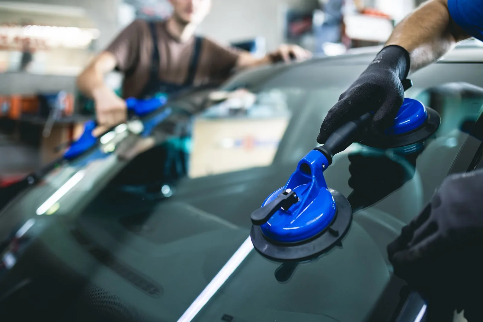 Technician using blue suction cups to lift vehicle windshield during auto glass replacement