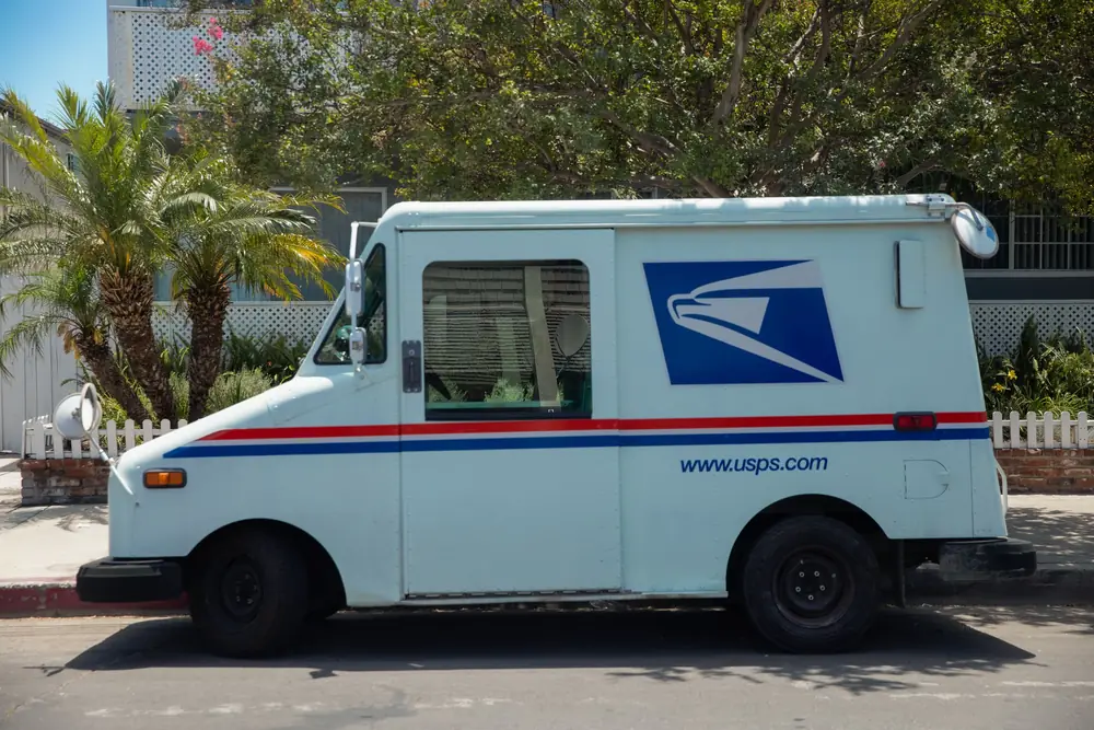 USPS mail delivery truck parked on street with palm trees in background
